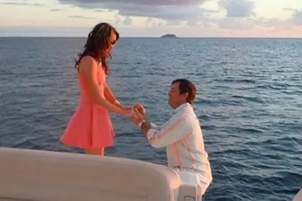 A man is proposing to a woman on a boat with the ocean and the horizon in the background