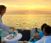 A server is pouring a beverage for a smiling woman on a boat during a sunset cruise with a child seated beside her looking on