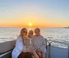 Three people are smiling and posing for a photo on a boat with a beautiful sunset over the water in the background