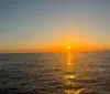 Three people are smiling and posing for a photo on a boat with a beautiful sunset over the water in the background