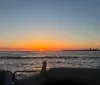 Three people are smiling and posing for a photo on a boat with a beautiful sunset over the water in the background