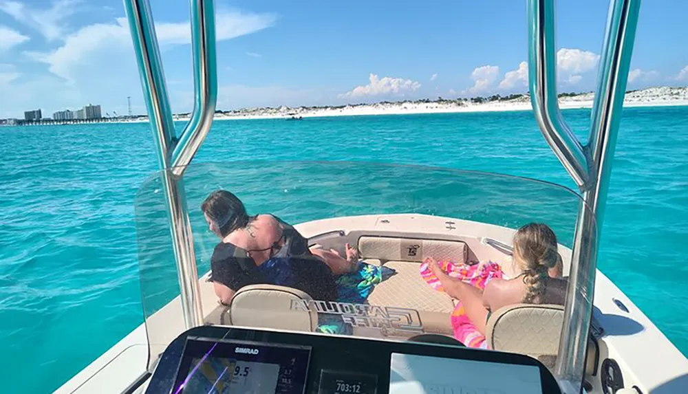 Two adults and a child are relaxing on a boat with clear turquoise waters in the background