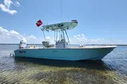 A turquoise center console boat is anchored in shallow water under a clear sky.