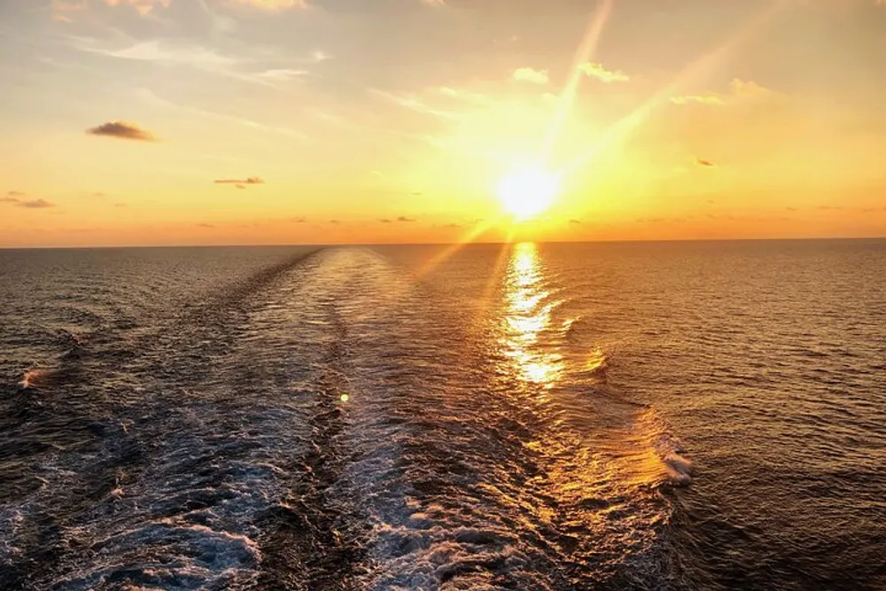 The image depicts a sunset over the ocean with the sun casting a warm glow on the water accompanied by the gentle wake of a boat