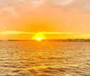 The image depicts a sunset over the ocean with the sun casting a warm glow on the water accompanied by the gentle wake of a boat