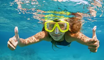 A person is giving two thumbs up while snorkeling underwater, wearing a yellow mask.