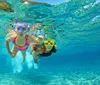 Two individuals are swimming underwater both wearing goggles with clear blue water surrounding them