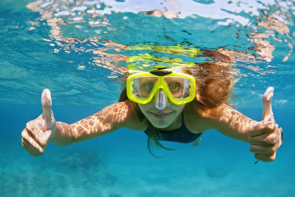 A person is underwater giving a thumbs-up while wearing a yellow snorkeling mask