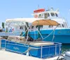 A blue and white pontoon boat named Emil Chaser is docked at a marina beside a larger vessel with clear skies in the background