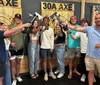 A group of smiling people are posing for a photo while holding axes at an indoor axe-throwing venue