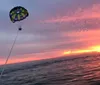 Two people are parasailing above the ocean towed by a boat that is moving swiftly across the water