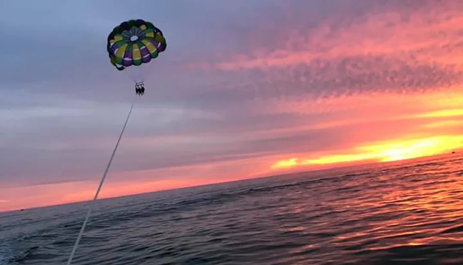 A colorful parachute carries people parasailing at sunset above the ocean.