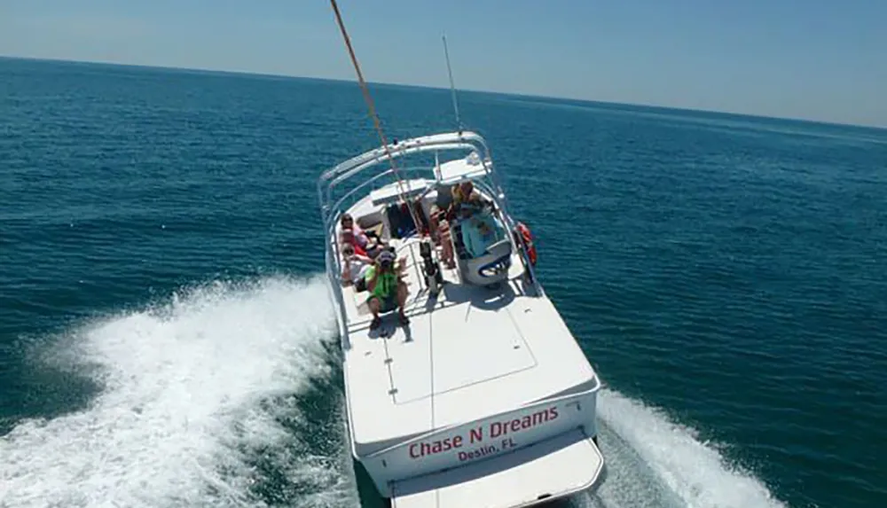 A group of people is enjoying a sunny day on a white powerboat named Chase N Dreams cruising on the blue sea