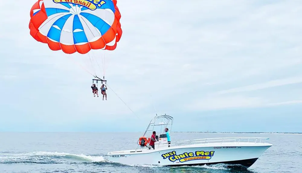 Two people are parasailing above the ocean towed by a boat that is moving swiftly across the water
