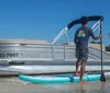 A person stands on a paddleboard near a pontoon boat on a calm water surface suggestive of a leisurely day at the beach
