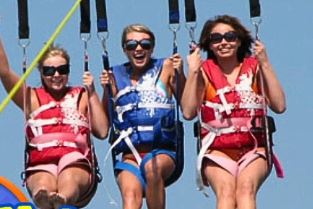 Three people are wearing life jackets and enjoying a parasailing adventure against a clear blue sky