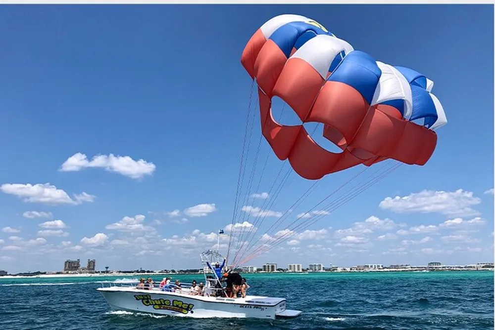 A parasail with a colorful canopy is flying above the water tethered to a boat filled with people enjoying their time at sea