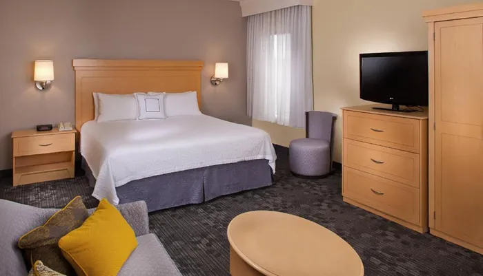 The image shows a neatly arranged modern hotel room with a large bed a television a sitting area and a minimalist decor