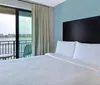 A modern bedroom with a large bed facing a balcony that offers a view of a water body and the distant skyline