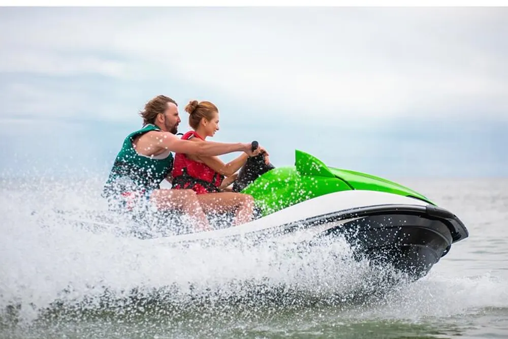 Two people are riding a green and black jet ski on the water making a spray as they speed along