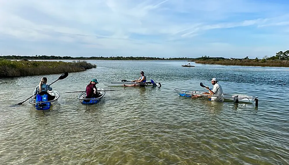 People are paddling in small individual watercrafts on a calm waterway surrounded by a natural landscape under a partly cloudy sky