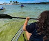 A person is paddling a transparent kayak over clear water offering a view of the underwater environment