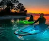 A person in a straw hat is kayaking on a calm water body during a beautiful sunset