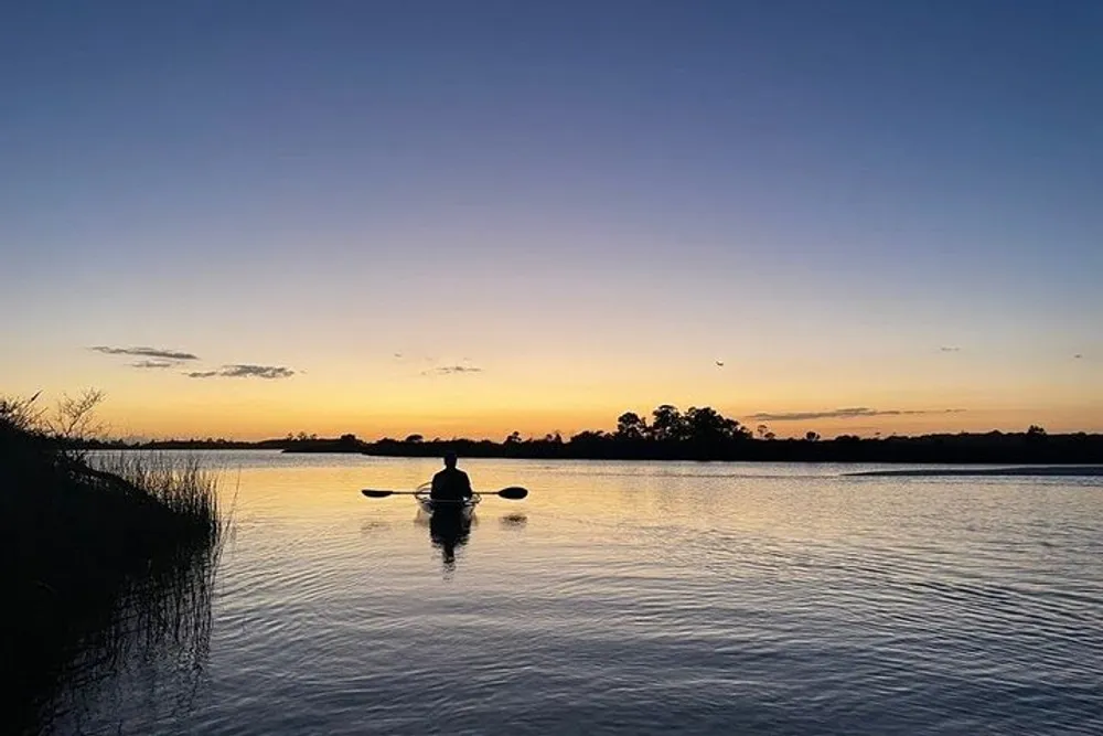 A person kayaks on tranquil waters against the backdrop of a beautiful sunset