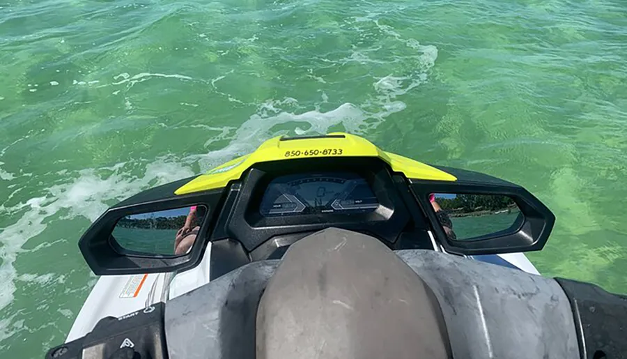 The image shows a first-person view from a jet ski rider cruising over green-tinted water, with the dashboard and handlebars of the jet ski visible in the foreground.