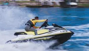 A person is riding a yellow and black jet ski on the water at high speed.