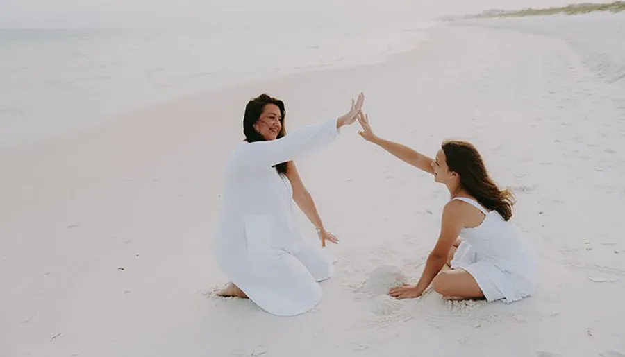 Two people are on a beach giving each other a high-five, with the water and horizon in the background.