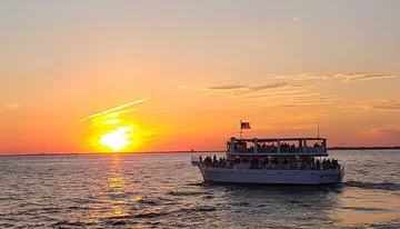 A tour boat is filled with passengers as they enjoy a vivid sunset over the water.