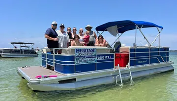 A group of people enjoys a sunny day on a pontoon boat on calm waters with other boats in the background.