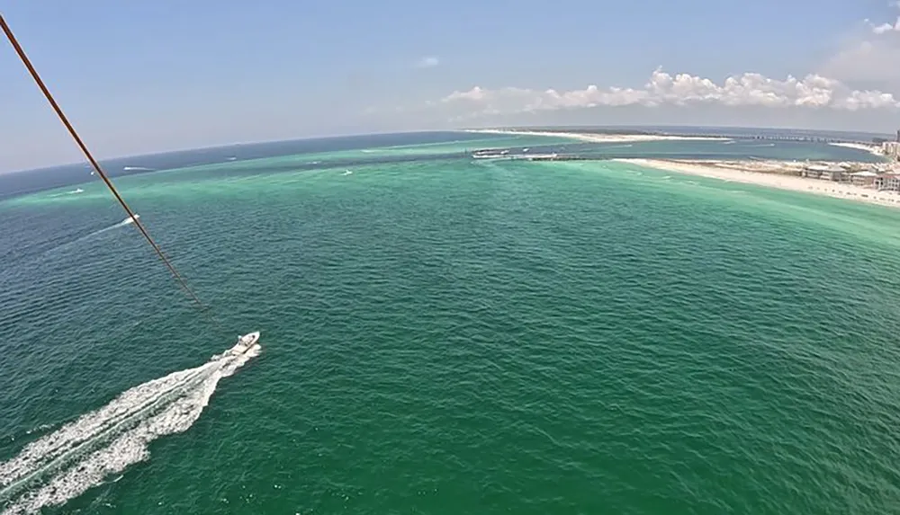 The image shows a panoramic view of a turquoise sea with a boat creating a white wake viewed from a parasail with its rope entering the frame from the top left corner