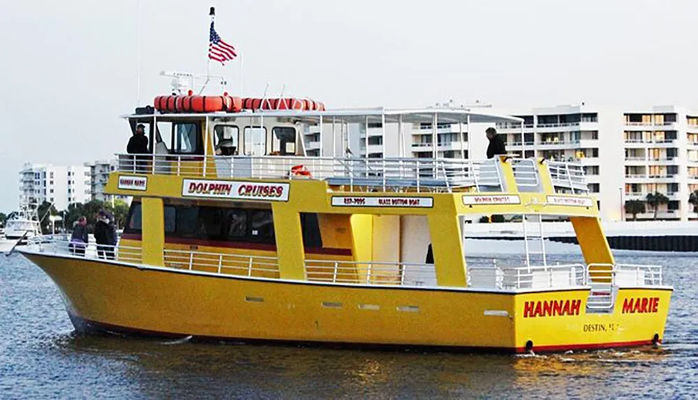 A yellow boat named Hannah Marie offers dolphin cruises sailing near buildings with a few passengers visible on deck and an American flag flying at the stern