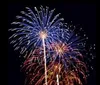 A girl smiles for the camera with a man beside her while other people watch fireworks at night