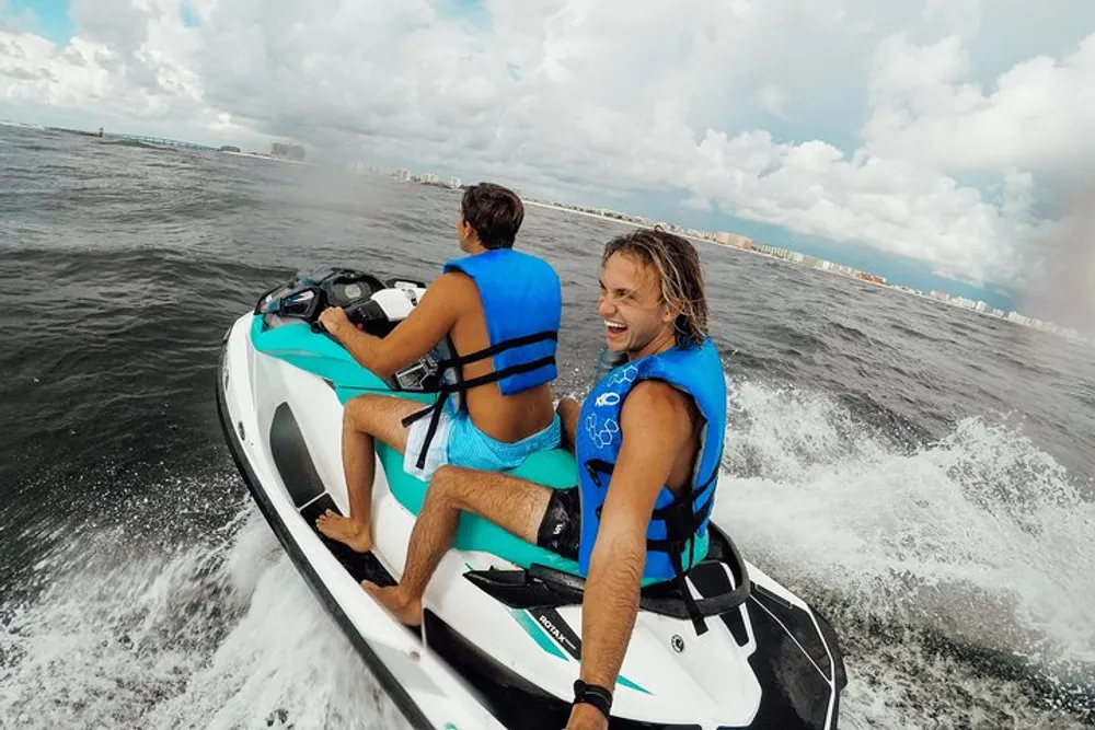 Two people are riding a jet ski on a body of water smiling and enjoying themselves as they speed along with one of them looking back at the camera