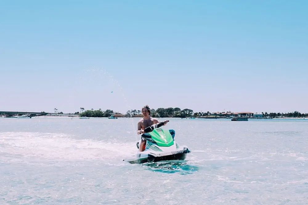 A person is riding a jet ski across a calm body of water under a clear blue sky