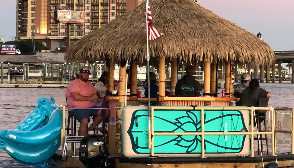 A group of people enjoys drinks on a floating tiki bar boat at dusk