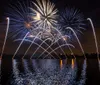 A vibrant fireworks display reflects on a body of water at night
