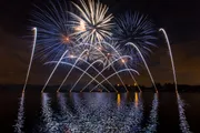 A vibrant fireworks display reflects on a body of water at night.