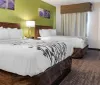 The image shows a tidy and modern hotel room with two beds featuring white linens with black floral patterns a desk with a chair and green and purple wall art above each bed