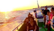 Passengers are enjoying a sunset boat ride on the ocean with a warm glow from the setting sun reflecting on the water.