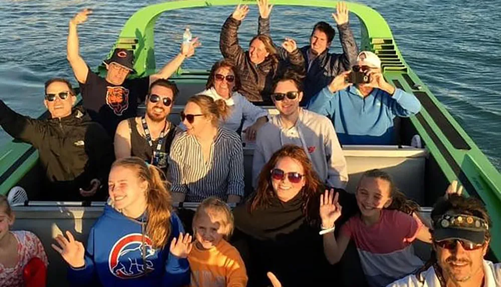 A group of people are smiling and waving at the camera while enjoying a boat ride in sunny weather