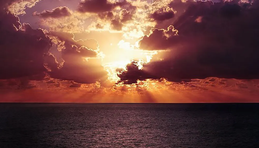 The image shows a dramatic sunset over the ocean with the suns rays piercing through the clouds
