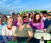 A group of joyful people are posing with excited expressions while seated on what appears to be a bright green boat with a clear sky and water in the background