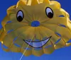 A group of people is parasailing with a bright yellow smiley-faced parachute against a clear blue sky