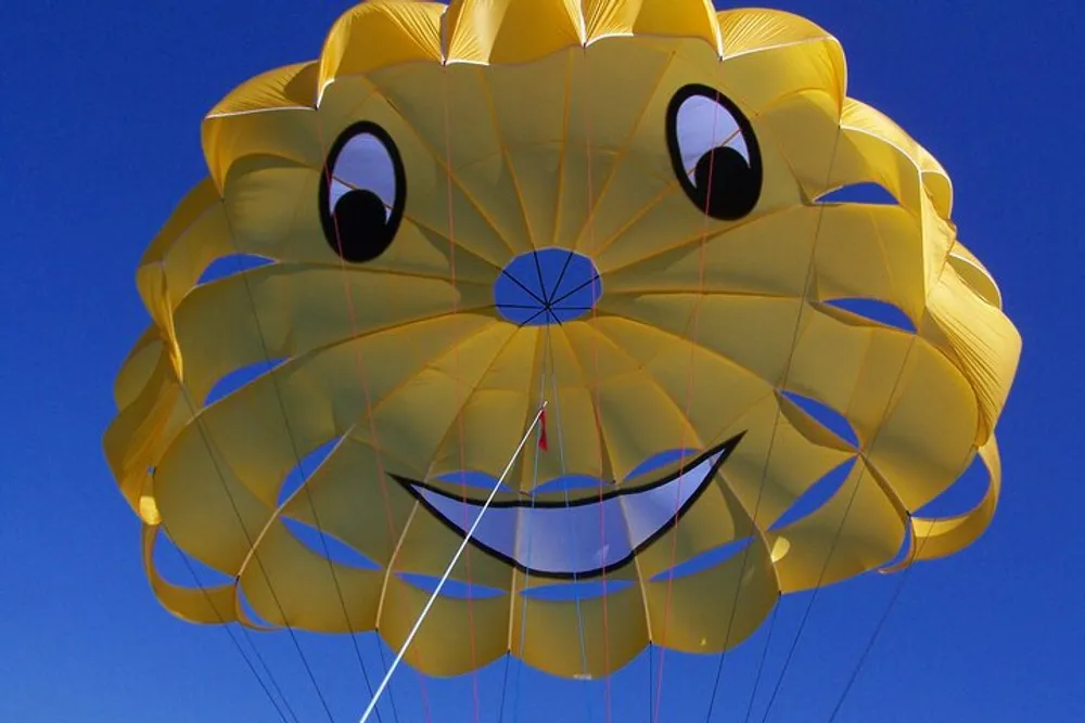 A yellow smiling parasail with a cartoon face is set against a clear blue sky