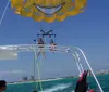 A group of people is parasailing with a bright yellow smiley-faced parachute against a clear blue sky