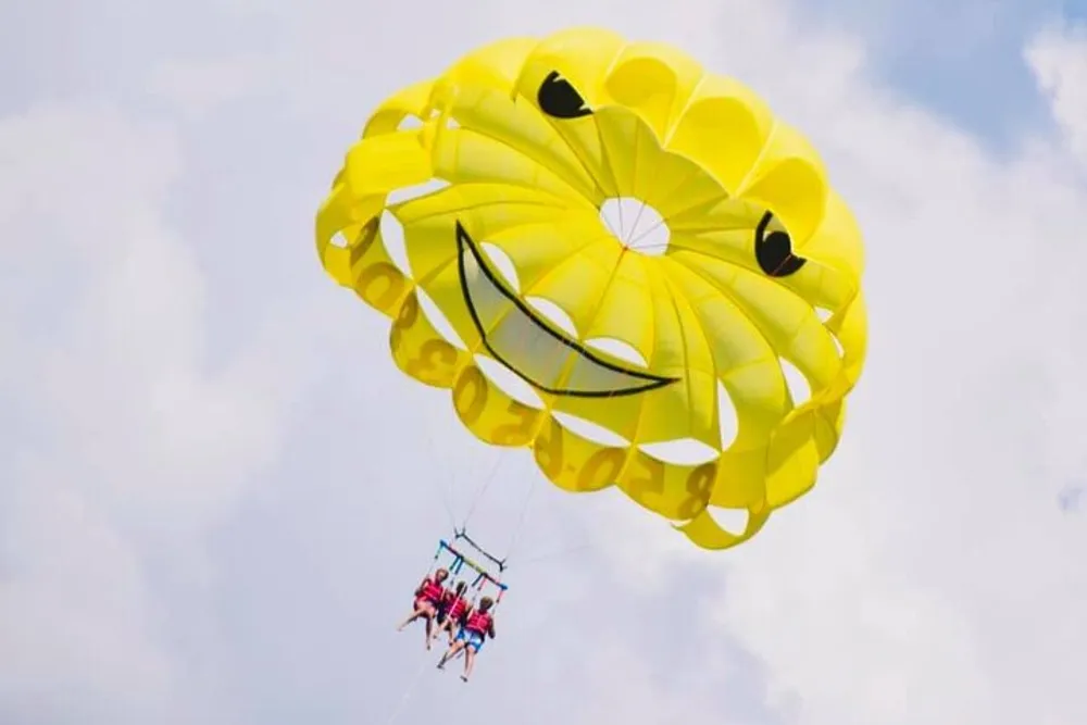 A group of people is parasailing with a bright yellow smiley-faced parachute against a cloudy sky
